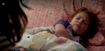 a little girl laying in bed with a blanket