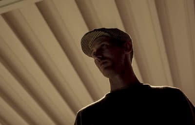 a man wearing a hat standing in front of a window