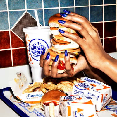 a woman holding a giant hamburger over a tray of food