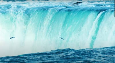 two birds flying over a large waterfall in the ocean
