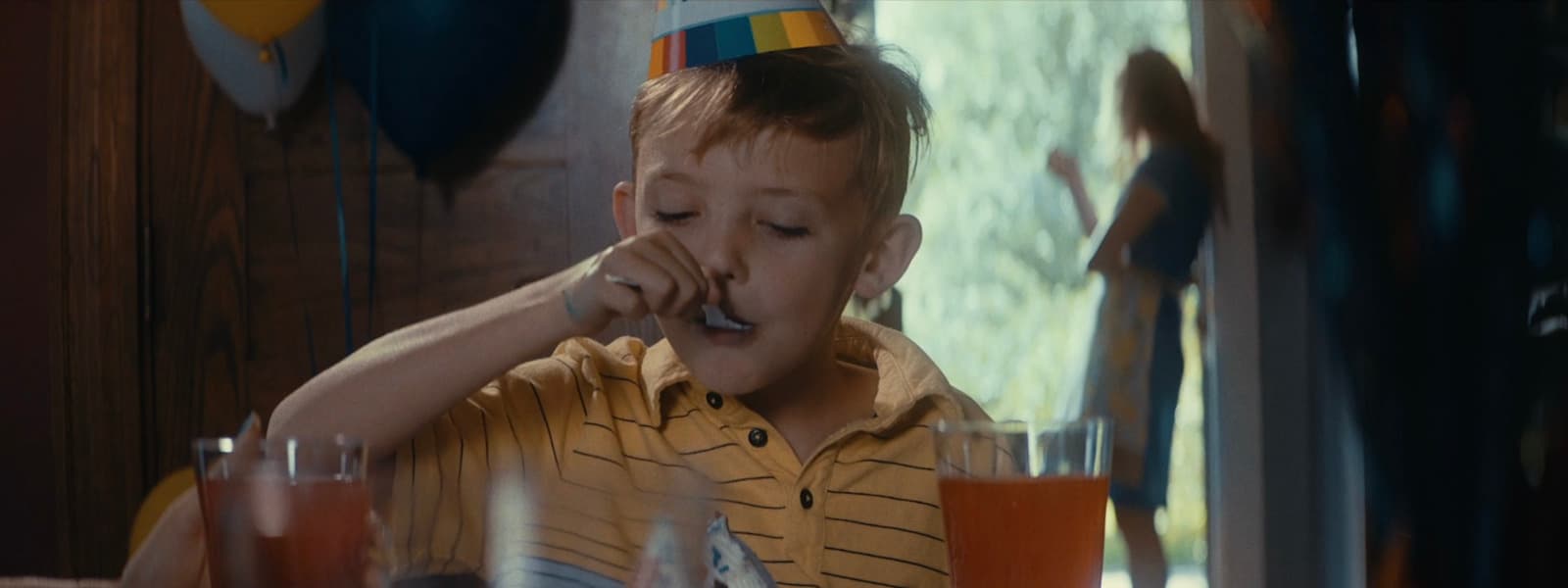 a young boy sitting at a table with a party hat on