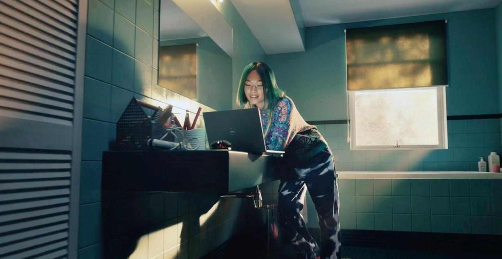 a woman standing in a bathroom using a laptop computer