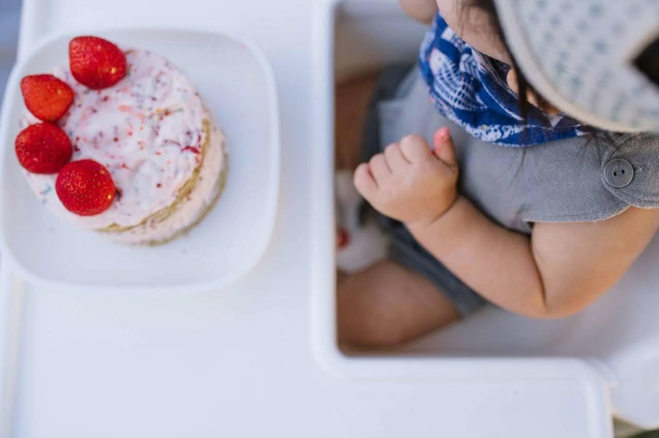 a small child sitting on a white table with a plate of food