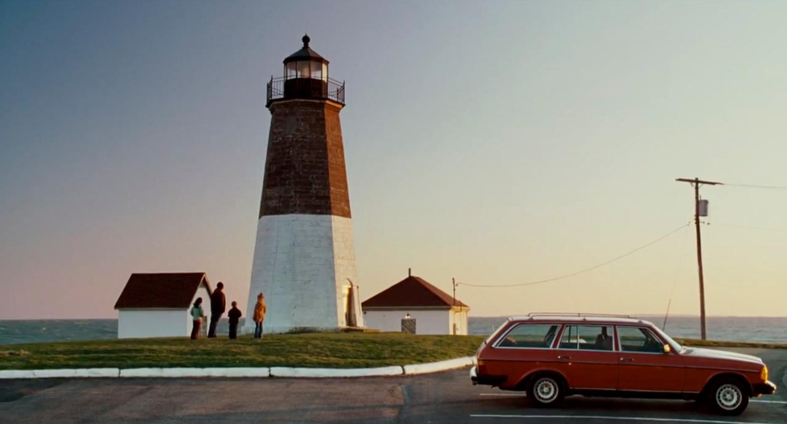 a red car parked in front of a light house