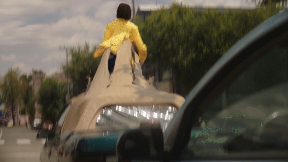 a man in a yellow shirt jumping off a car