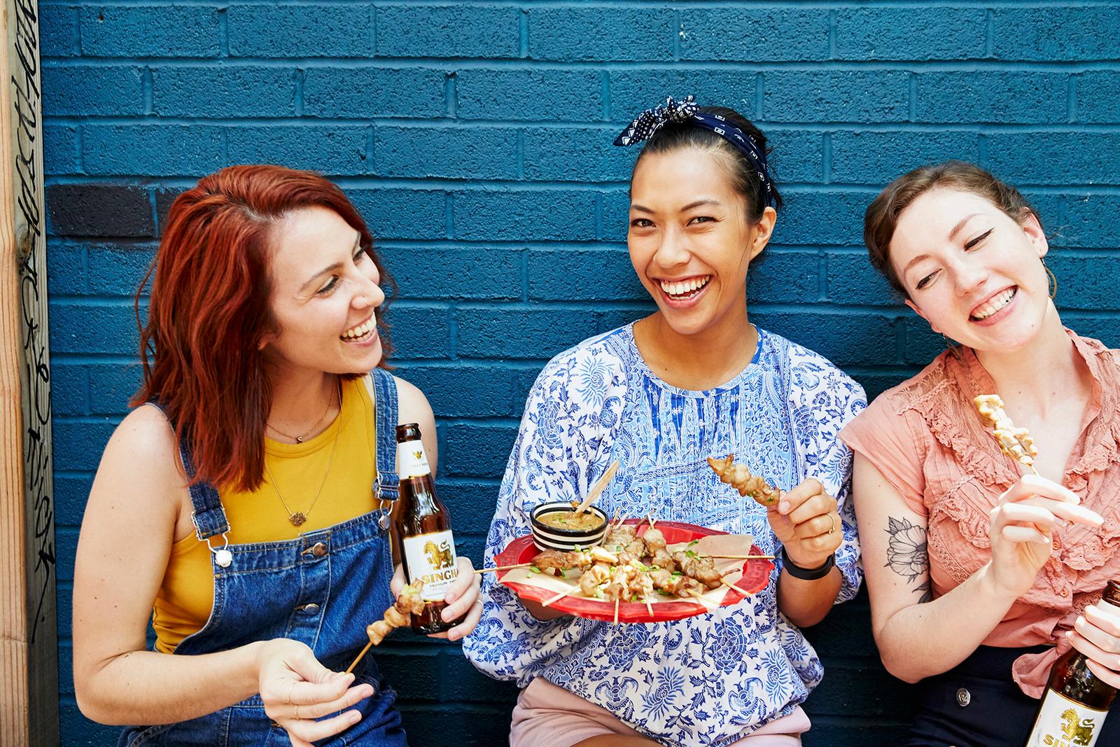 three women sitting on a bench eating food and drinking beer