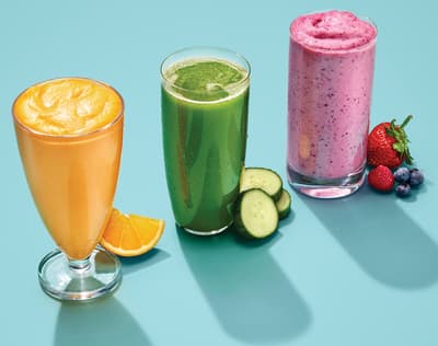 three glasses of smoothie, a cucumber, a strawberry, and a