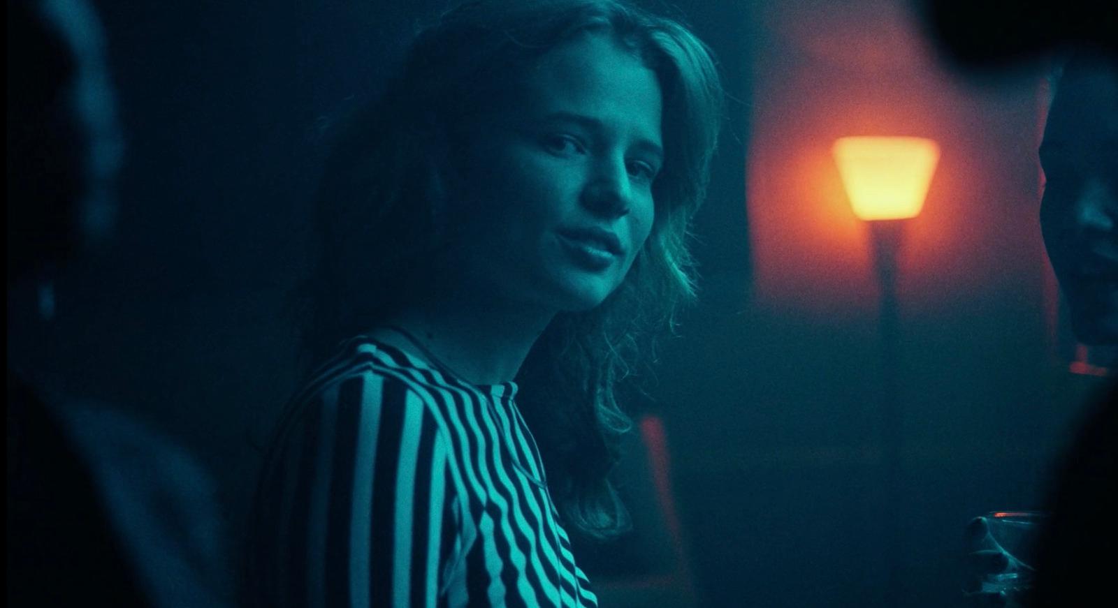 a woman standing in a dark room next to a lamp