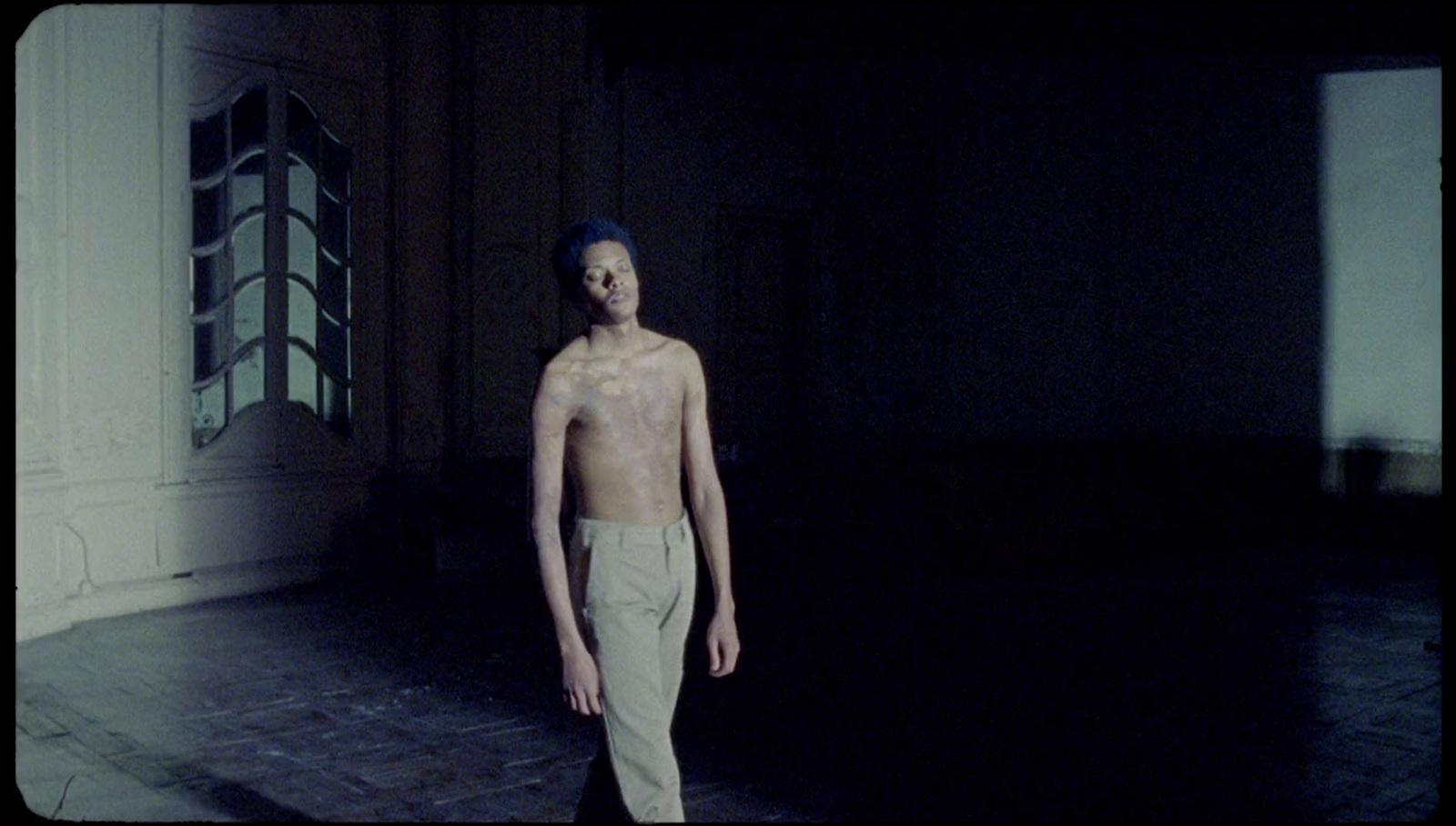 a man without a shirt standing in a dark room