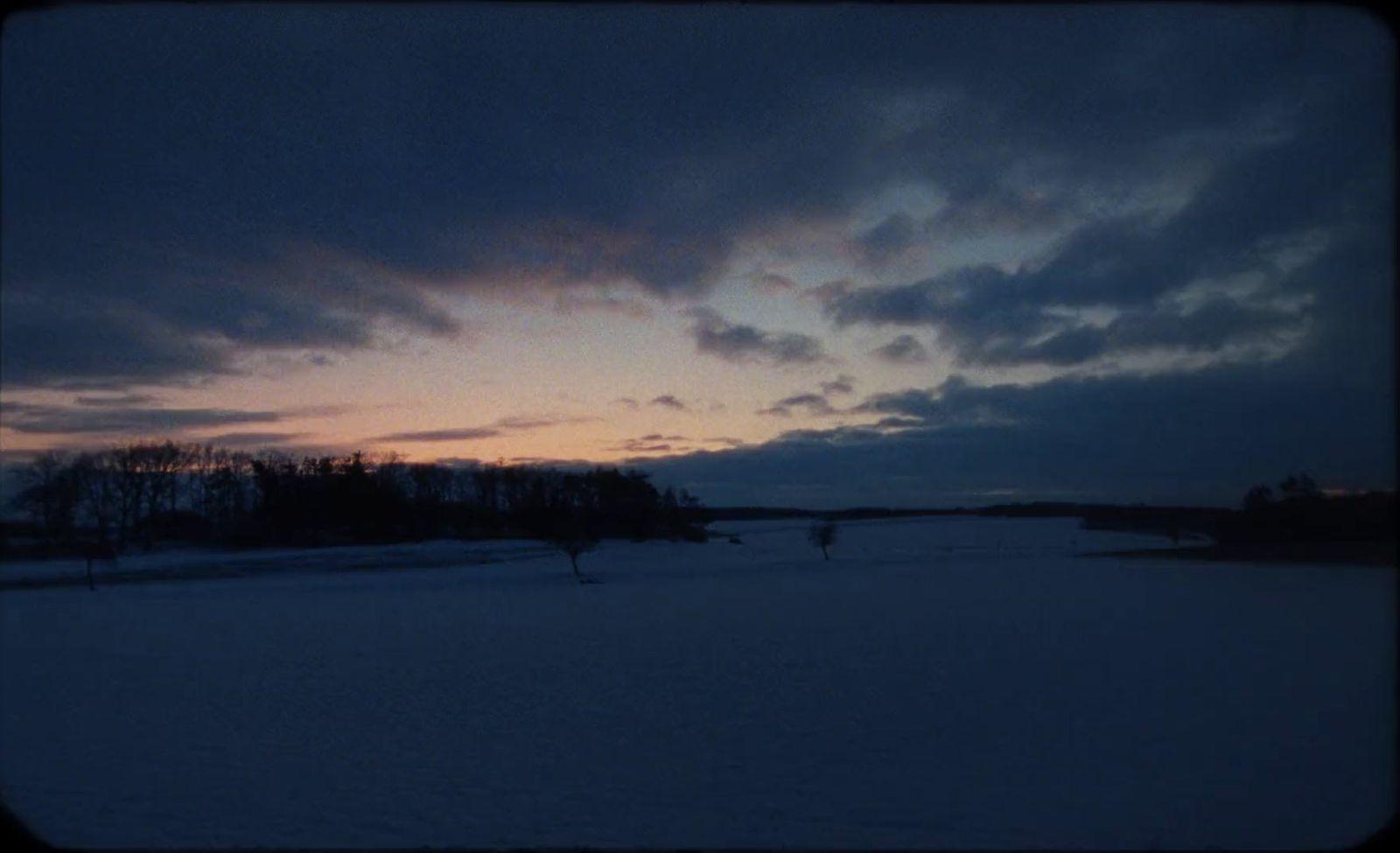 a snowy field with trees and a sky in the background