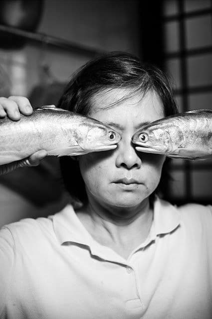 a woman holding two fish over her eyes