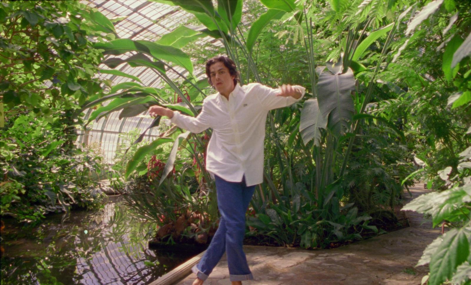 a man in a white shirt and blue pants standing in a greenhouse