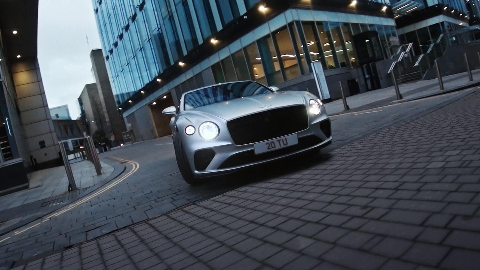 a silver car driving down a street next to tall buildings