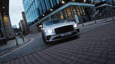 a silver car driving down a street next to tall buildings