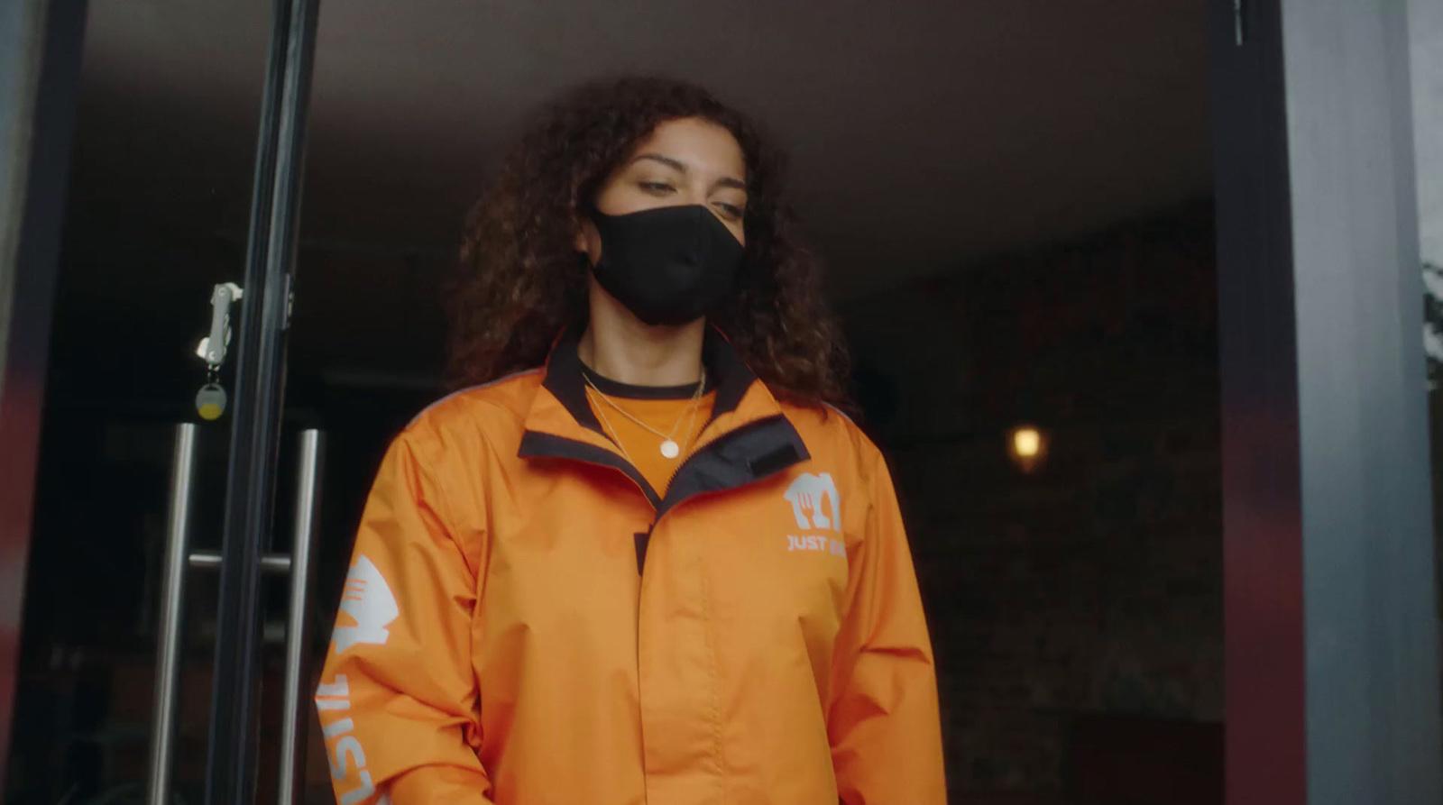 a woman wearing an orange jacket and a black face mask