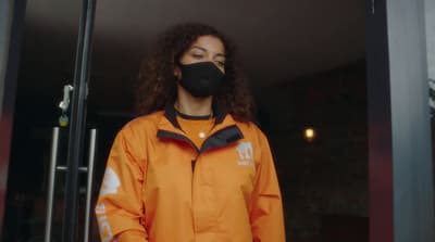 a woman wearing an orange jacket and a black face mask