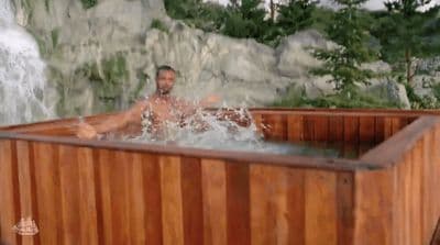 a man sitting in a wooden hot tub next to a waterfall