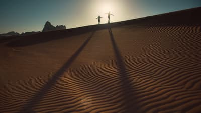 a couple of people standing on top of a sandy hill