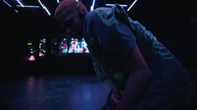 a man in a dark room with a video screen in the background