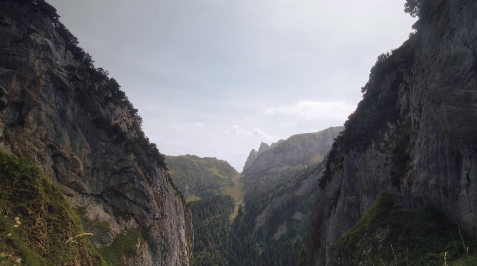a narrow river surrounded by mountains under a cloudy sky