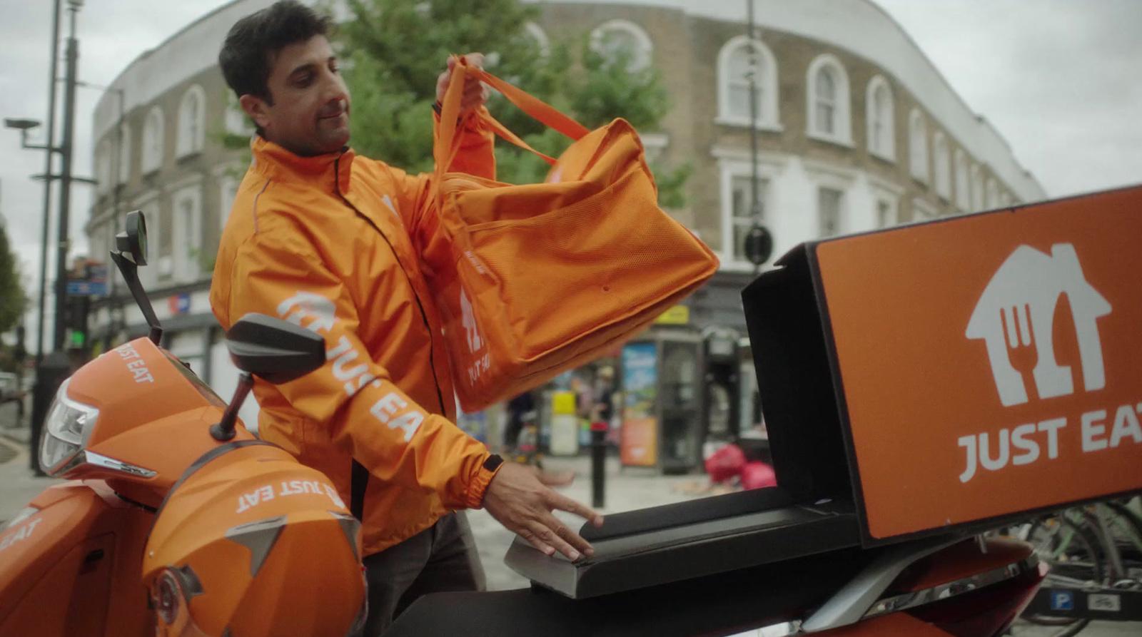 a man in an orange jacket standing next to a motor scooter
