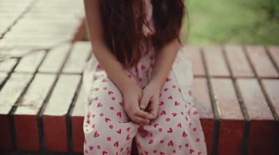 a girl sitting on a bench with her hands on her knees
