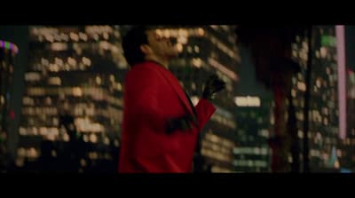 a man in a red suit standing in front of a city at night