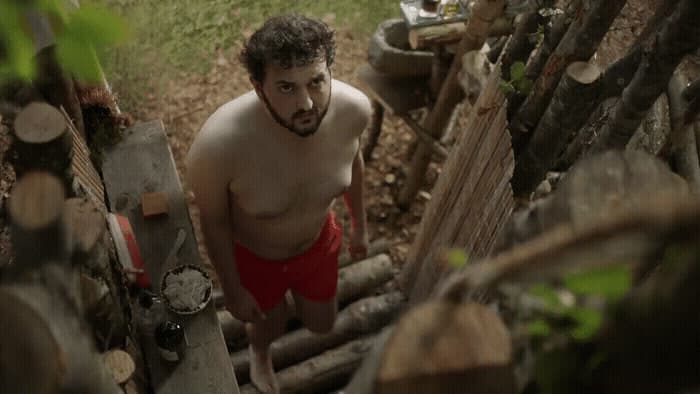 a shirtless man in red trunks standing in a yard