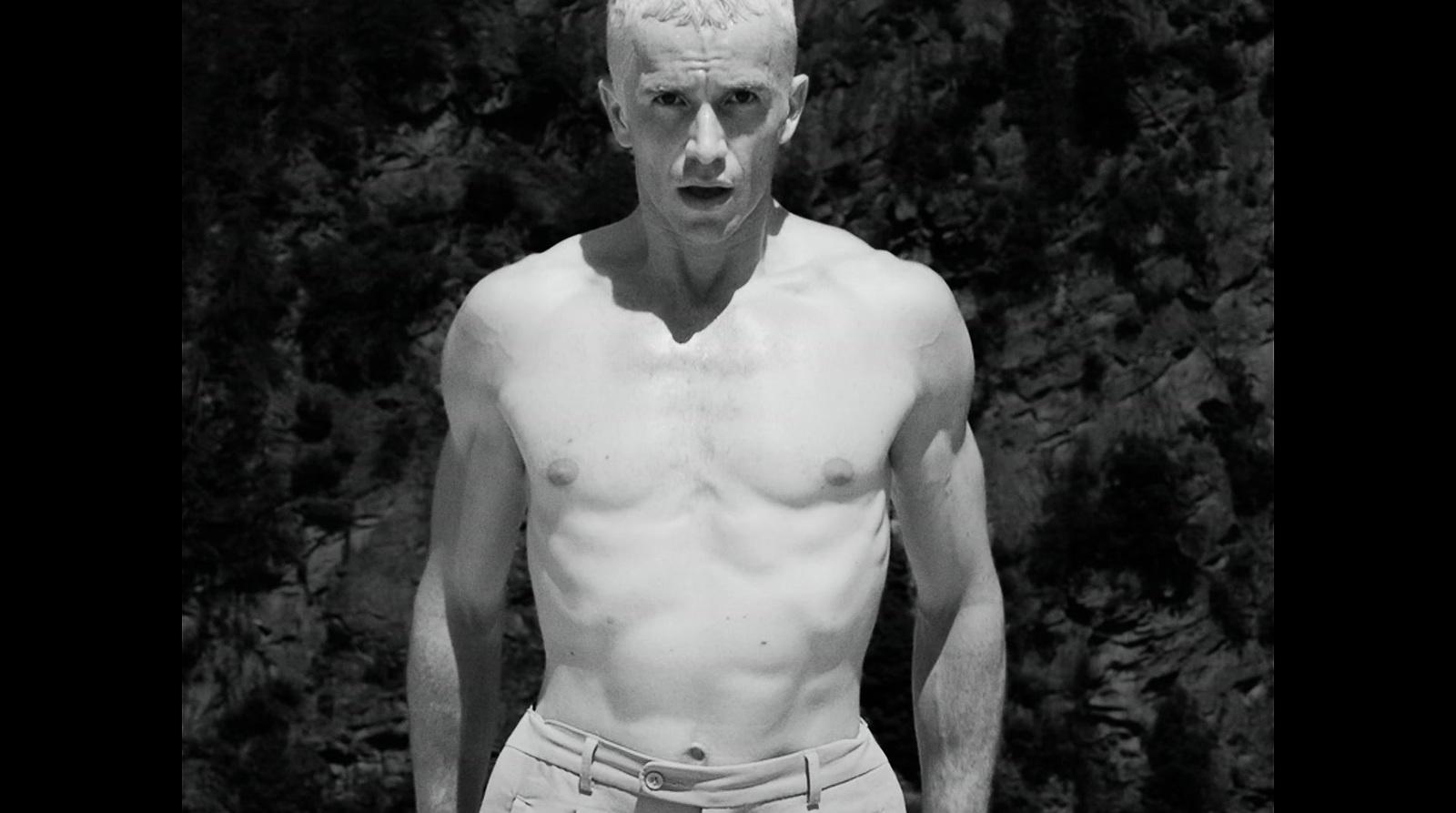 a man with no shirt standing in front of a tree