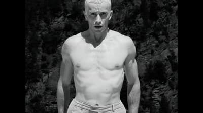 a man with no shirt standing in front of a tree