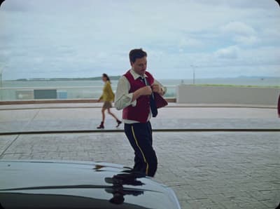 a man in a maroon vest is standing on the hood of a car