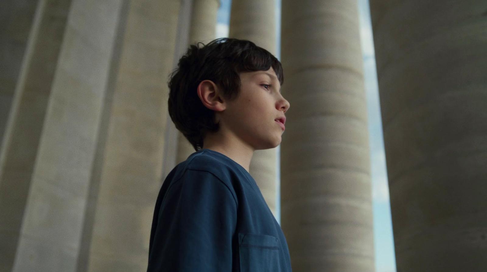 a young boy standing in front of columns