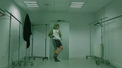 a man standing in a white room with a green hoodie
