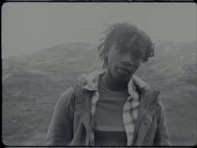a man with dreadlocks standing in front of a mountain