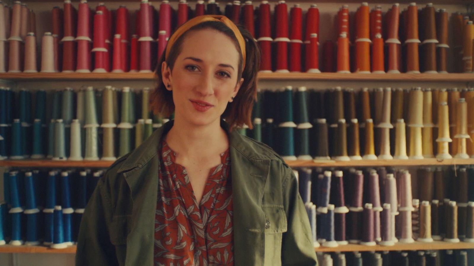 a woman standing in front of a wall of different colored spools of thread
