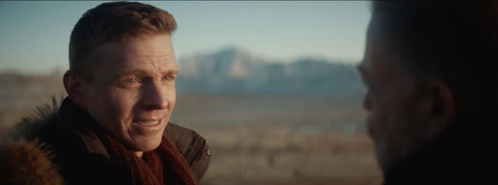 a man talking to another man with a mountain in the background