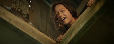a young girl is smiling while looking out from a wooden structure