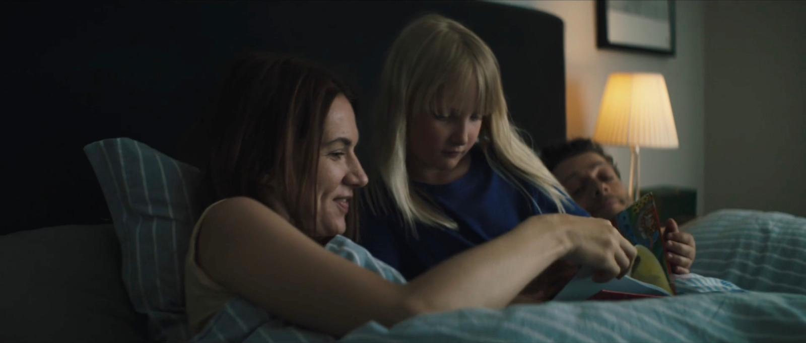 two women sitting on a bed looking at a book