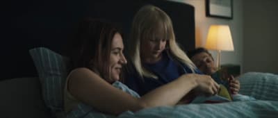 two women sitting on a bed looking at a book