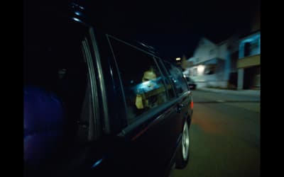 a man in a car driving down a street at night