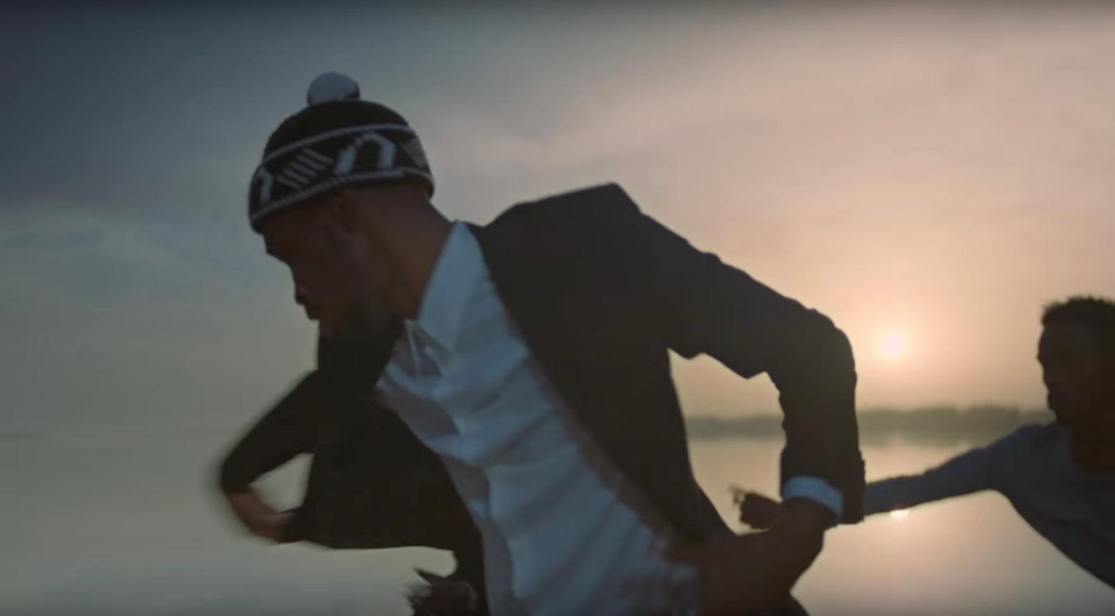 a man in a suit and hat running on the beach