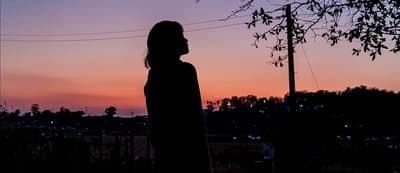 a silhouette of a person standing in front of a sunset