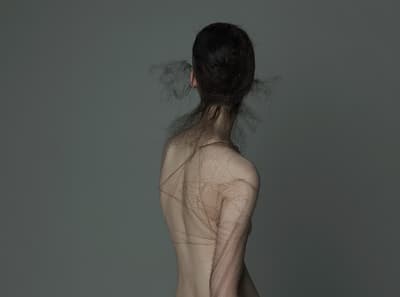 a woman with no shirt standing in front of a gray wall