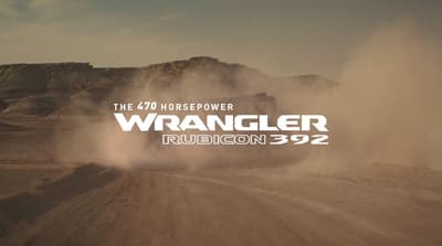 a truck driving down a dirt road next to a mountain