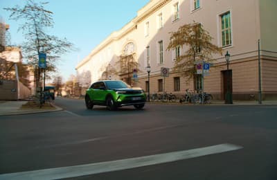 a green suv driving down a street next to a tall building