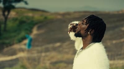 a man with dreadlocks standing in front of a hill