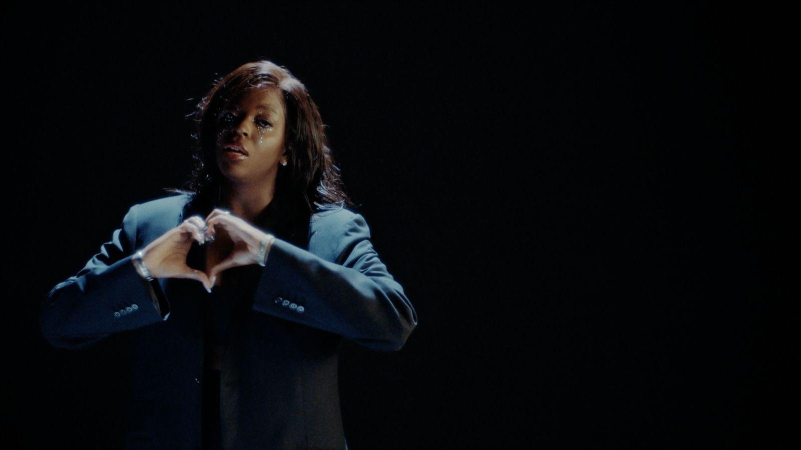 a woman standing in the dark making a heart with her hands