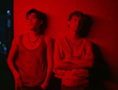 two young men standing in front of a red wall
