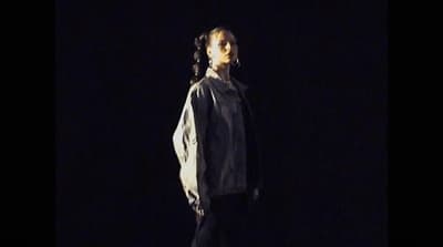 a man standing in the dark with his hair in a bun