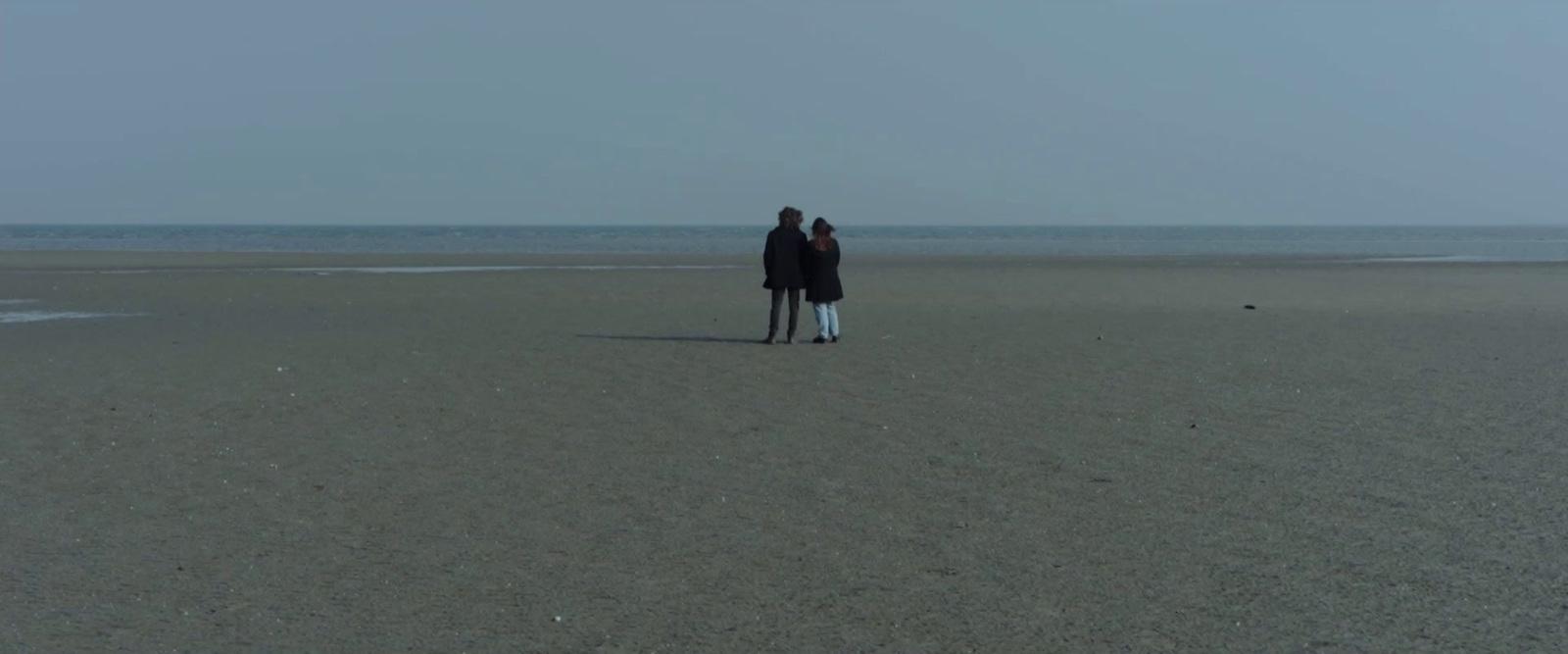 a man and a woman standing on a beach next to the ocean